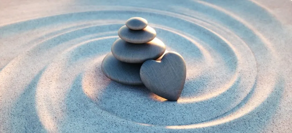 Herzförmiger Stein mit Steinstapel im Sand – Symbol für den Herzpunkt eines Raumes